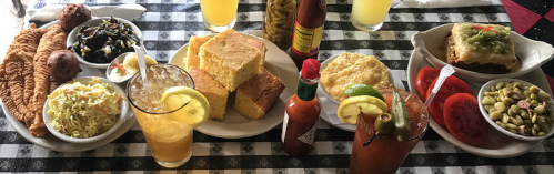 A vibrant spread of dishes including fried fish, cornbread, coleslaw, and various sides on a checkered tablecloth.