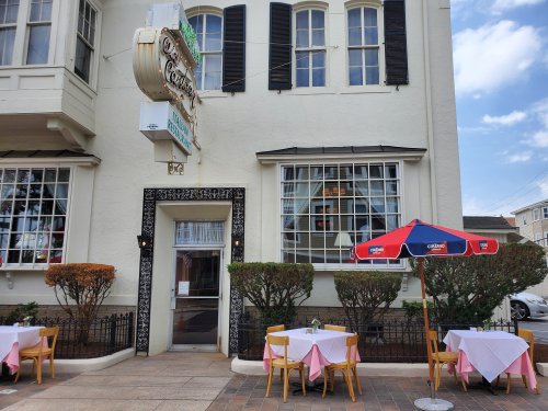 Exterior of a restaurant with a sign, outdoor seating, and a colorful umbrella on a sunny day.