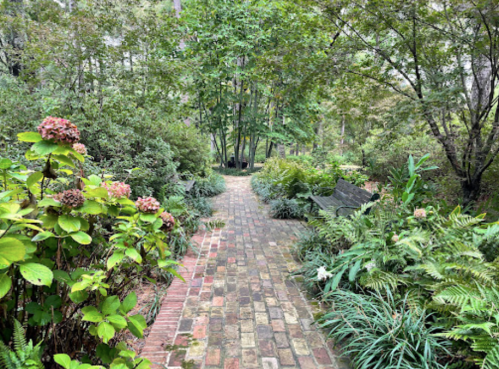 A winding brick path through a lush garden filled with greenery and blooming flowers.