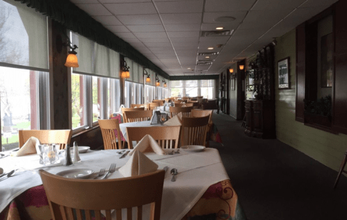 A spacious restaurant interior with tables set for dining, large windows, and warm lighting.