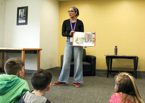 A person reads a book to a group of children sitting on the floor in a cozy indoor setting.