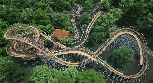 Aerial view of a wooden roller coaster winding through a lush green forest.