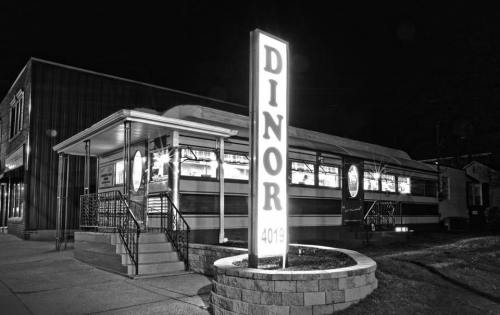 A vintage diner at night, illuminated by a bright sign reading "DINOR," with a classic architectural style.