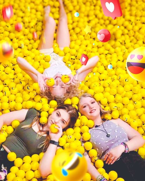 Three friends lying in a sea of yellow balls, surrounded by playful emoji graphics, smiling and enjoying their time together.
