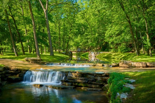 A serene landscape featuring a gentle waterfall surrounded by lush green trees and a peaceful stream.