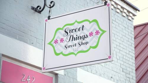 Sign for "Sweet Things Sweet Shop" with decorative elements, hanging from a building.