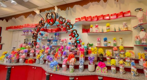 A colorful display of gift-wrapped treats and decorative jars on shelves in a festive shop.