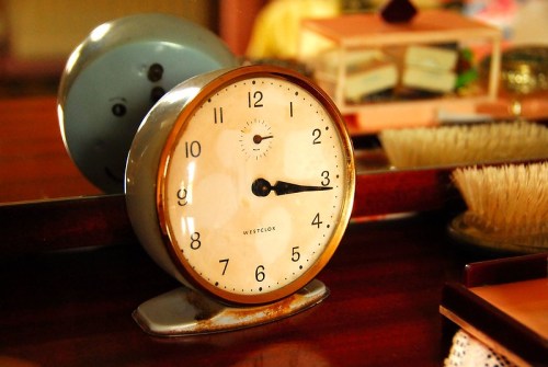 A vintage alarm clock with a white face and gold trim, resting on a wooden surface with soft lighting.