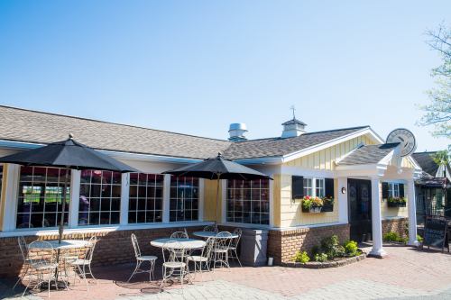A charming yellow restaurant with outdoor seating and umbrellas, set against a clear blue sky.