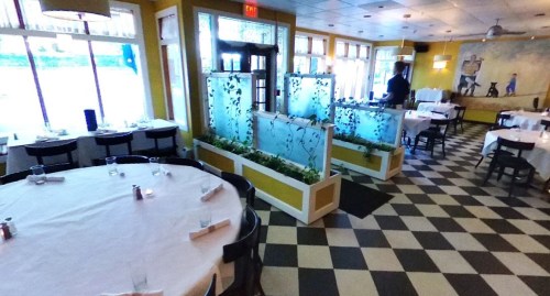 A bright restaurant interior with checkered floors, large windows, and fish tanks separating dining areas.