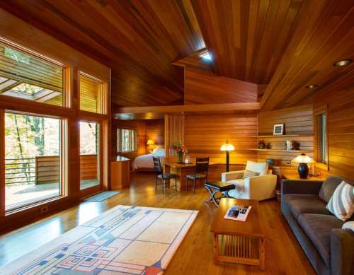 Cozy wooden interior of a modern cabin, featuring a living area with furniture, large windows, and warm lighting.