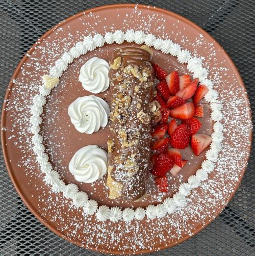 A dessert plate featuring a chocolate-covered cannoli, strawberries, and whipped cream, dusted with powdered sugar.