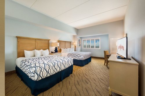 A hotel room featuring two beds, a desk, and a TV, with light blue walls and a cozy, inviting atmosphere.