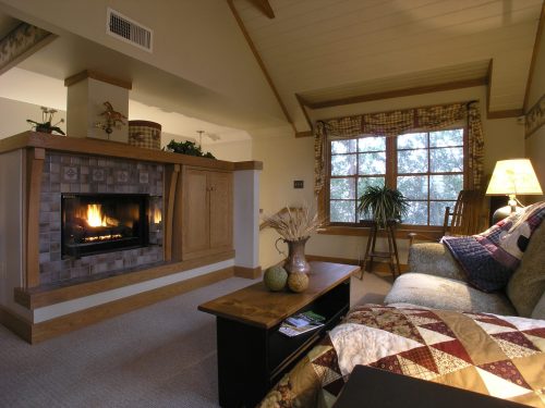 Cozy living room with a fireplace, quilted sofa, wooden coffee table, and large window overlooking trees.
