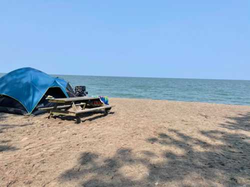 A sandy beach with a blue tent and a picnic table near the water under a clear sky.