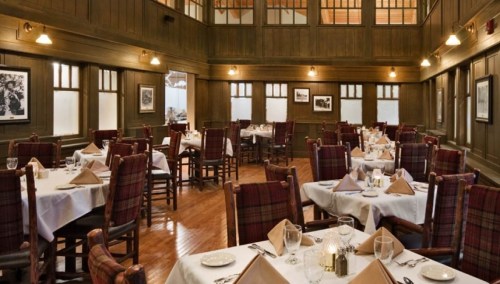 Elegant restaurant interior with wooden walls, tables set with white linens, and warm lighting.