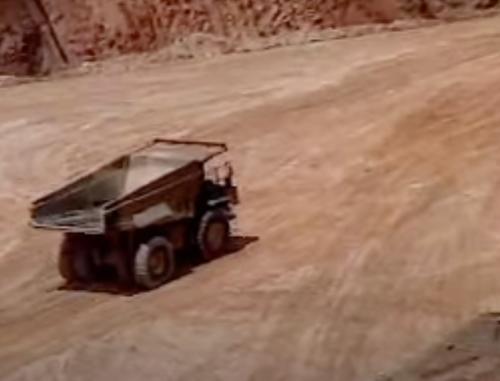 A dump truck drives on a dirt road in a construction or mining site.