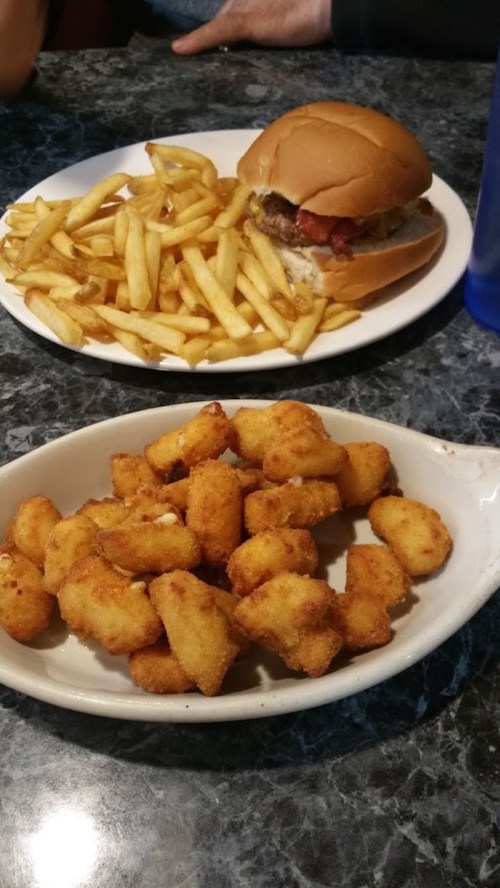 A plate with a burger and fries in the background, and a dish of golden, crispy bites in the foreground.