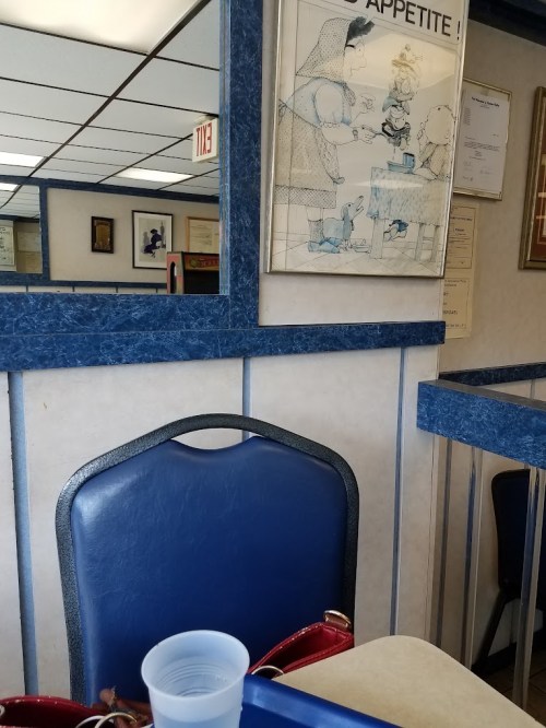 A blue chair and table in a diner, with a framed illustration on the wall and a cup of water on the table.