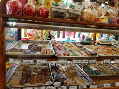A display case filled with various colorful candies and fudge, including chocolate and fruit flavors.