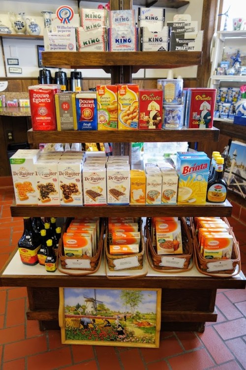 A wooden display shelf filled with various Dutch food products, including cookies, syrups, and beverages.