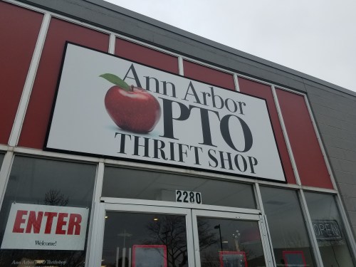 Sign for "Ann Arbor PTO Thrift Shop" featuring an apple logo, with an entrance door visible below.