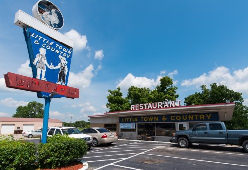 A restaurant named "Little Town & Country" with a vintage sign, surrounded by cars and trees under a blue sky.