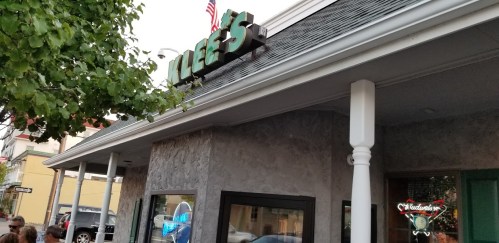 Sign for "Alice's" on a building exterior, with trees and a street visible in the background.