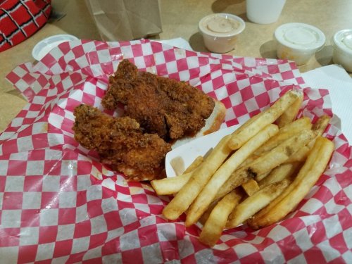 A plate of fried chicken strips and French fries on red and white checkered paper.
