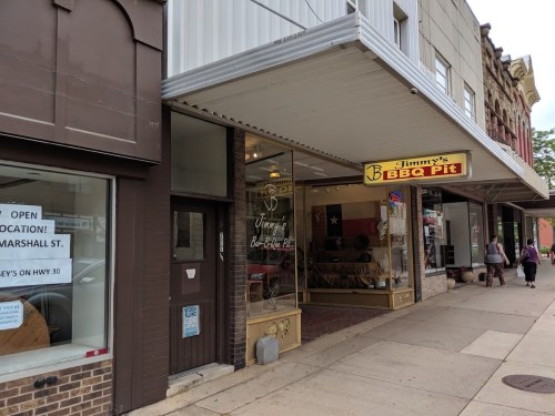 Exterior of Jimmy's BBQ Pit, featuring a sign and a Texas flag in the window, located on a city street.