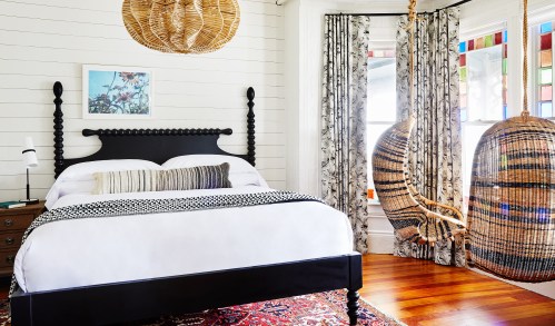 A cozy bedroom featuring a black bed, woven hanging chairs, colorful stained glass, and patterned curtains.