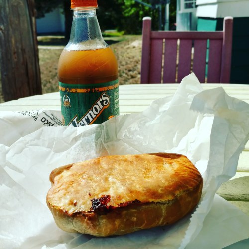 A savory pastry on a table next to a bottle of Vernors soda, wrapped in paper.