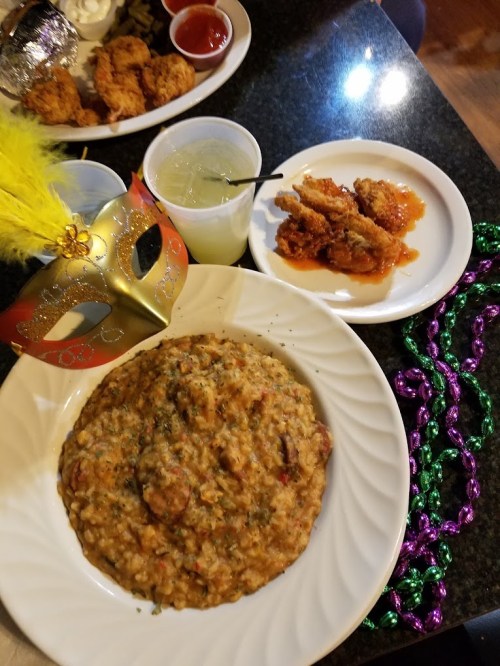 A plate of flavorful rice dish with herbs, a side of fried chicken, a drink, and a colorful mask on a festive table.