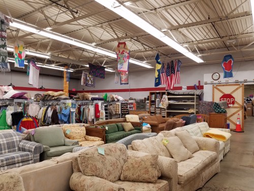 A spacious thrift store interior filled with various couches and clothing racks, decorated with colorful banners and flags.