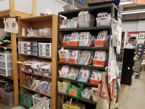A storage area with shelves filled with organized craft supplies and patterns in labeled bins and containers.