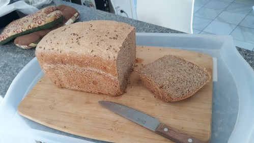 A loaf of whole grain bread on a cutting board, with a slice cut and a knife beside it.