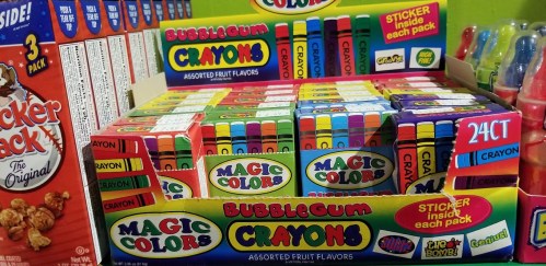 Colorful boxes of bubblegum-flavored crayons and sticker packs displayed on a shelf.