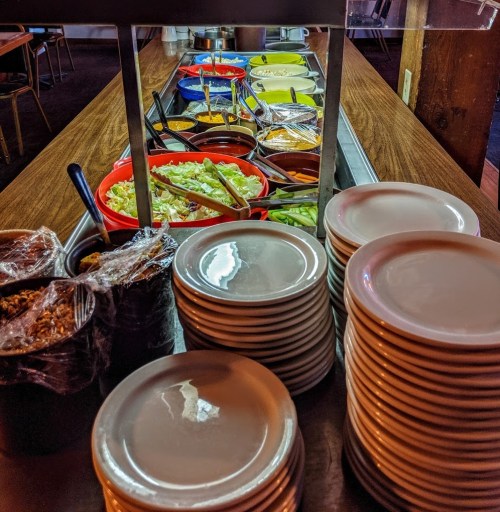 A buffet table with various colorful dishes, sauces, and fresh ingredients, alongside stacks of white plates.