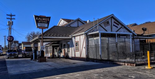 A storefront with a sign reading "Kalmes Store," featuring a covered outdoor area and parked cars nearby.
