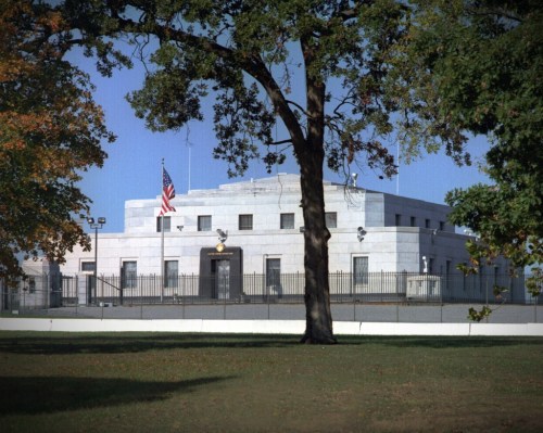 A large, round stone building with an American flag, surrounded by a fence and trees in a grassy area.