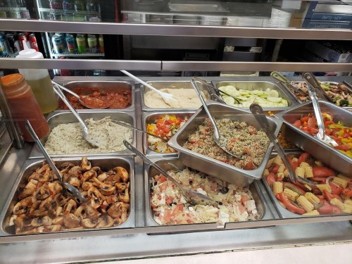 A variety of dishes in metal trays, including rice, vegetables, and sauces, displayed in a food service area.