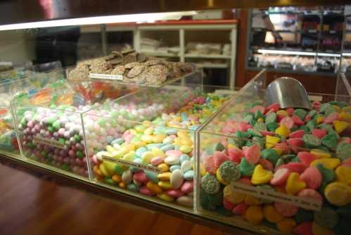 Colorful candy displayed in clear bins, featuring pastel shapes and smooth, vibrant pieces in a sweet shop setting.