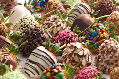 A variety of chocolate-covered strawberries decorated with sprinkles, nuts, and drizzles in an assortment of colors.