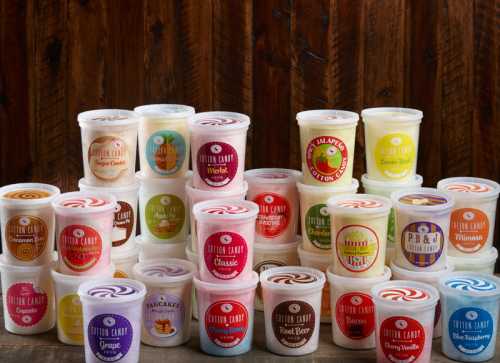 A colorful display of various cotton candy containers with unique flavors arranged on a wooden background.