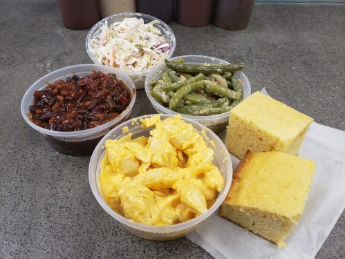 A spread of comfort food including macaroni and cheese, green beans, coleslaw, baked beans, and cornbread.