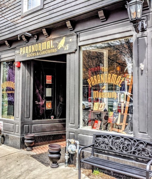 Exterior of the Paranormal Museum, featuring a sign and display of books and curiosities in the window.
