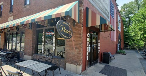 Exterior of a coffee shop with a striped awning, outdoor seating, and an American flag displayed.