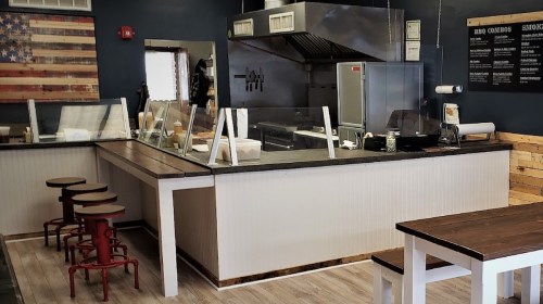 Interior of a BBQ restaurant featuring a service counter, stools, and a wall with an American flag design.