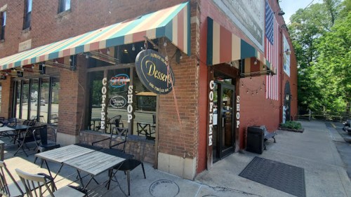 A cozy dessert shop with outdoor seating, featuring a striped awning and an American flag on the adjacent building.