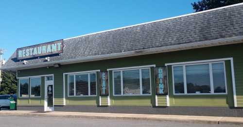 A green restaurant building with a shingled roof, featuring large windows and signs that say "EAT" and "DRINK."